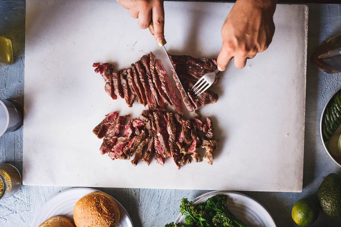 Person cutting beef grill steak in sliced over marble kitchen table overhead hot beef grilled steak