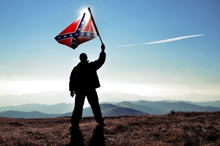 successful silhouette man winner waving Confederate flag on top of the mountain peak
