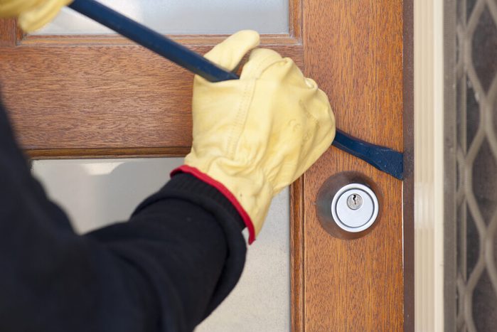 Burglar, thief with gloves, holding crowbar breaking into home, unlock door, copy space.