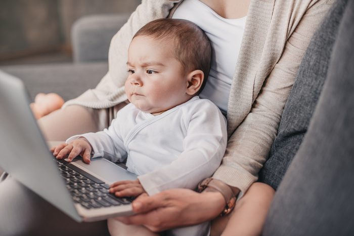 Closeup portrait of little boy with funny facial expression sitting on mother's knees and exploring laptop