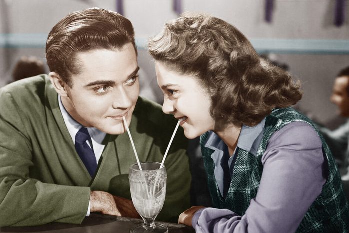 Couple in a restaurant looking at each other and sharing a milk shake with two straws