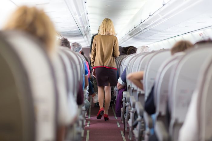 Interior of airplane with passengers on seats and stewardess walking the aisle.