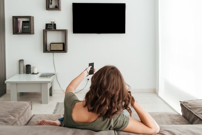 Back view of casual woman sitting on sofa and watching TV in home