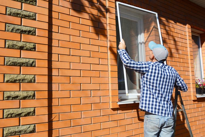 Worker installing mosquito net or mosquito wire screen on brick house window.
