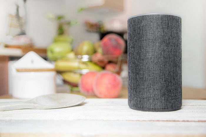 Personal assistant connected loudspeaker on a wooden table in a Smart Home in a kitchen. Next, some utensils, food and fruit. Empty copy space for Editor's text.