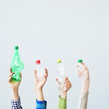 Hands holding crushed plastic bottles upward against a plain background.