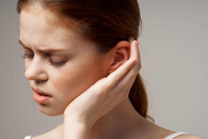 woman with closed eyes holds hand near ear 