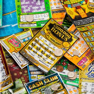 Scratch-off lottery tickets scattered, featuring coins atop, in a colorful, varied layout with visible prizes and text.