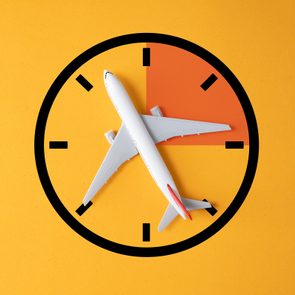 Airplane positioned as clock hand, suggesting flight time, on a yellow background with a clock face design.