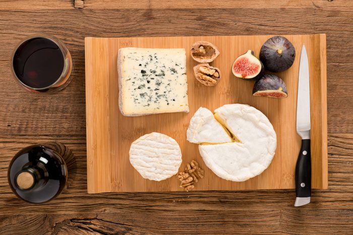 above overhead view flat lay assortment of various cheese with traditional bread fruits glass and bottle of red wine on old wooden table