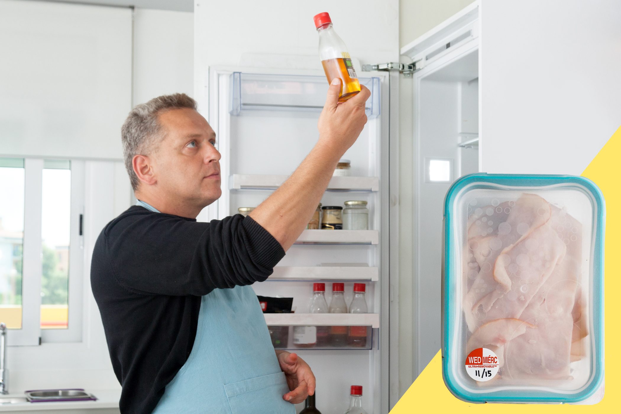 Man examines sauce bottle from refrigerator, wearing blue apron; container of sliced meat labeled "WED MÃ‰RC 11/15" on yellow background beside him.