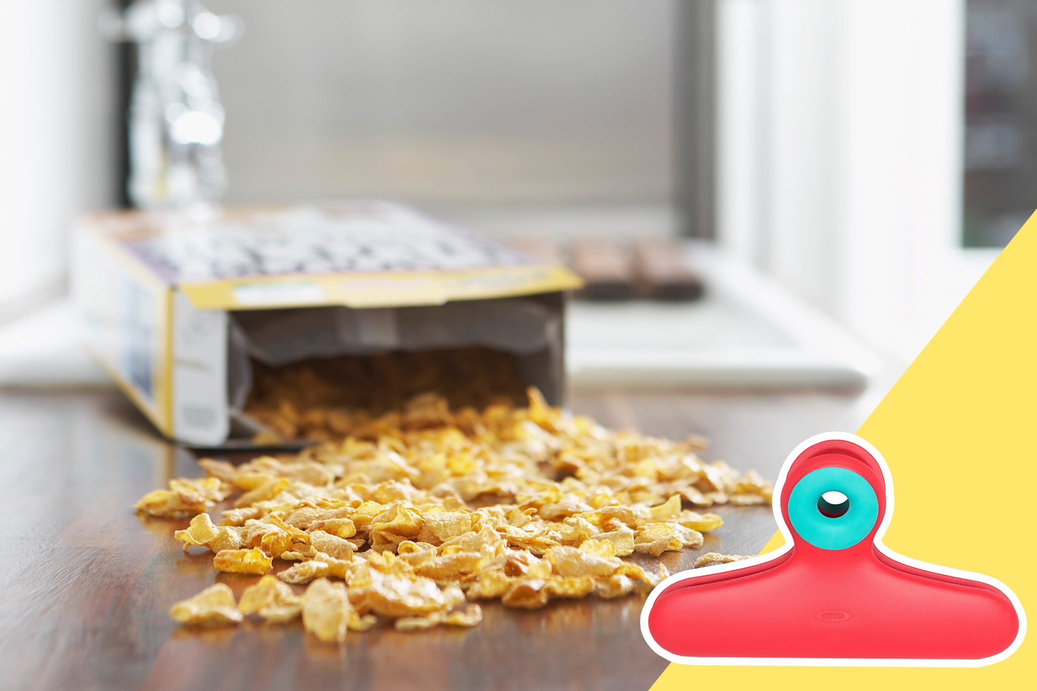 Cereal spills from an open box onto a wooden table; a red and turquoise clip is highlighted beside.