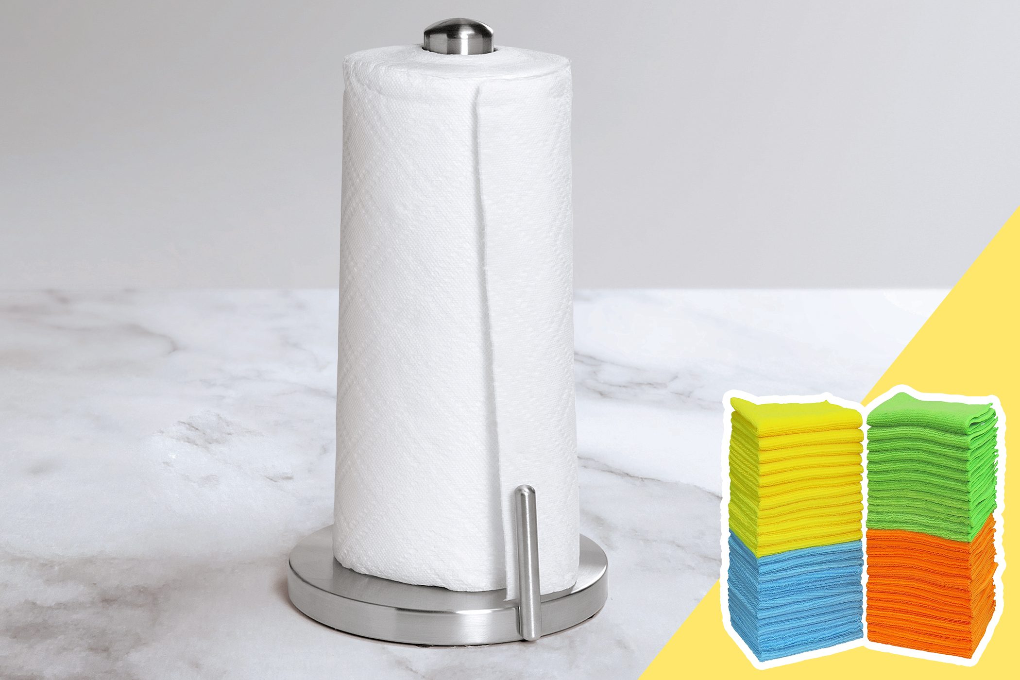 Paper towel roll stands upright on a metal holder on a marble surface; colorful cloth stacks sit on a yellow background.