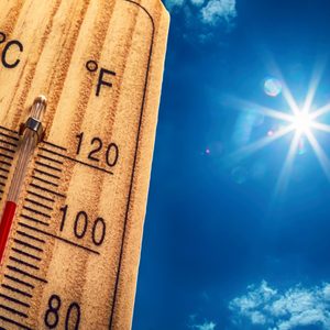 Thermometer showing high temperature, reaching around 100Â°F, against a bright, sunny sky with scattered clouds.