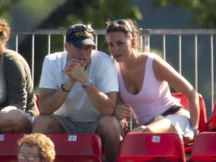 Two people sit closely, conversing in red stadium seats, surrounded by other spectators.