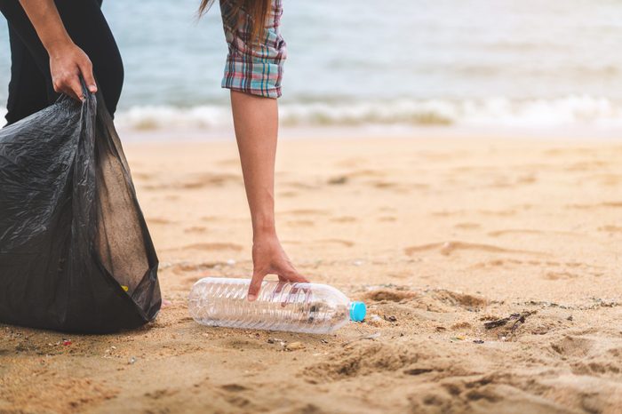 Asian woman picking bottle into plastic bag black for cleaning the beach in morning time, Volunteer concept.