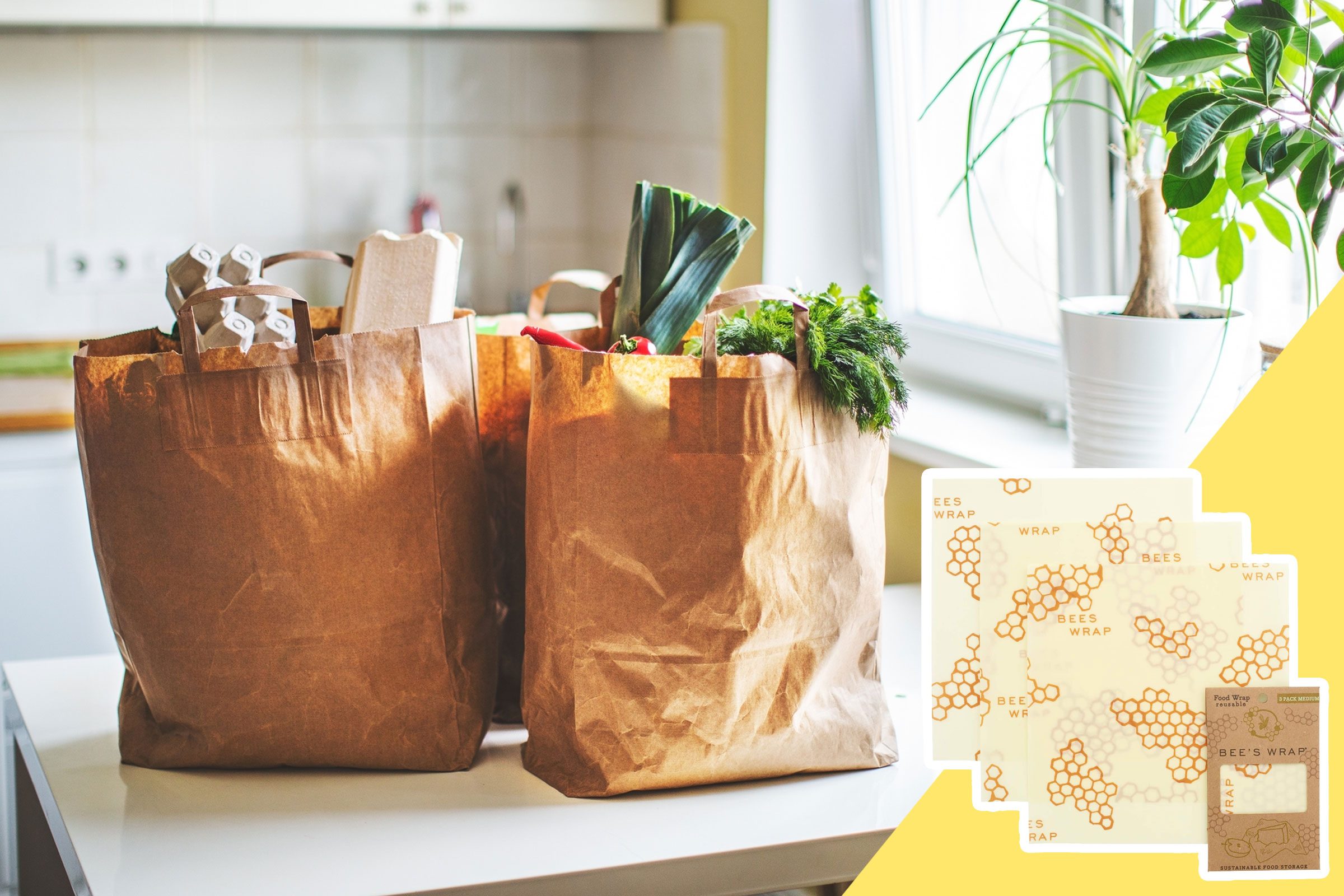 Paper bags holding groceries sit on a kitchen counter, with Bee's Wrap packaging displayed nearby and a potted plant in the background.