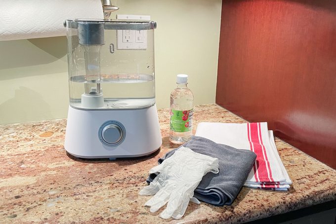 humidifier on kitchen counter next to cleaning supplies; vinegar, towel, gloves