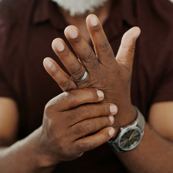 Hands clasped together, one wearing a ring and watch, in a casual setting.