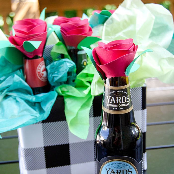 Bottles topped with paper roses are arranged in a checkered container, surrounded by colorful tissue paper.