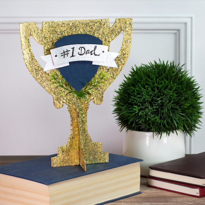 Glittery trophy decorates, resting on books near green plant on wooden surface. Text: 
