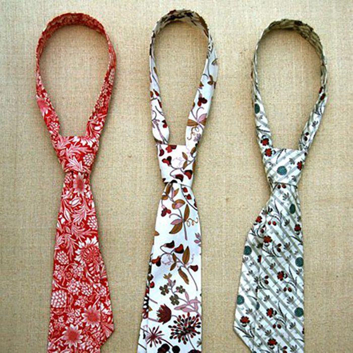 Three patterned neckties hang vertically against a textured beige background. Each tie features distinct floral designs in red, brown, and green hues.