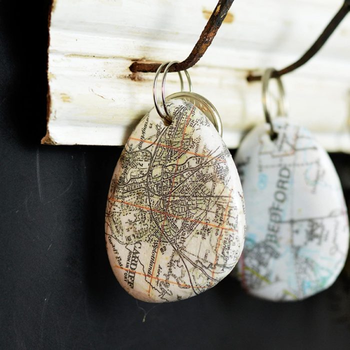 Teardrop-shaped keychain displaying a vintage map hangs from a rustic hook against a dark background.