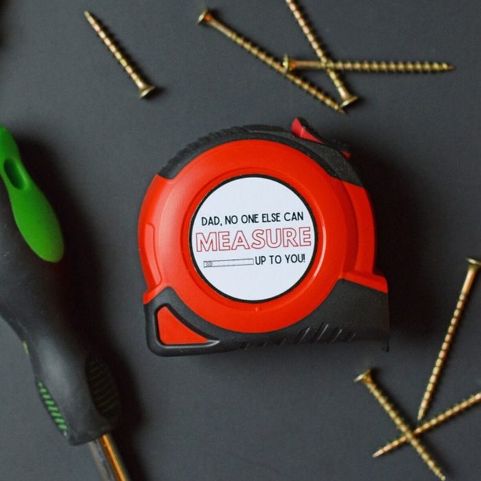 Tape measure resting surrounded by screws and screwdriver. Text reads, â€œDad, no one else can measure up to you!â€
