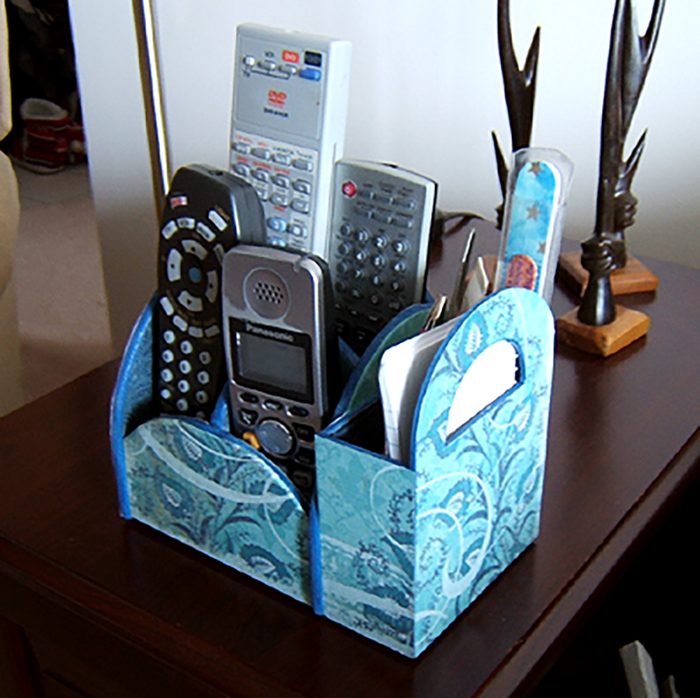 Organizer holds multiple remote controls on a wooden table, surrounded by blue floral-patterned sections and decorative antler ornaments nearby.