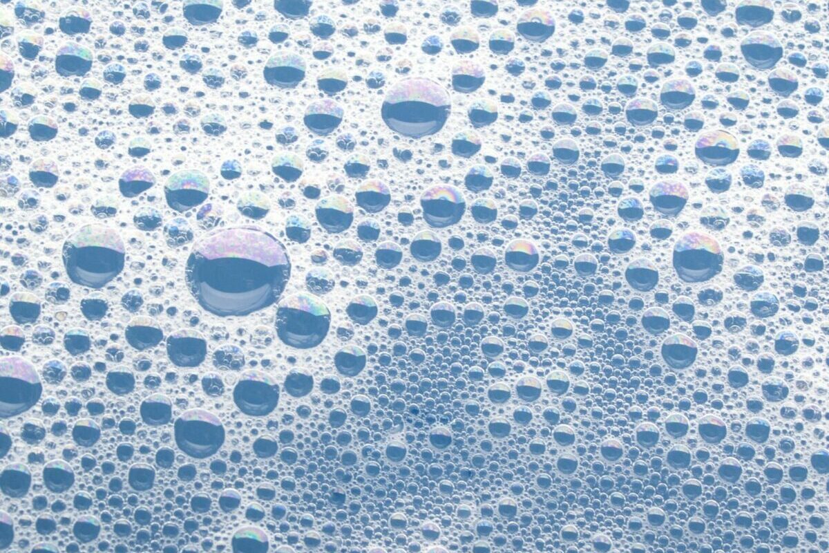 Bubbles cluster together, creating a foamy pattern on a light blue watery surface.