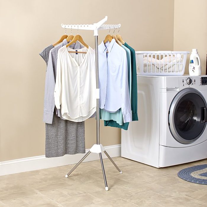 Clothing rack holds shirts on hangers, standing in a laundry room next to a washing machine and basket.