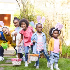 Children wearing costumes, carrying baskets, and smiling in a garden, enjoying a playful outdoor gathering.
