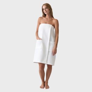Woman standing, wrapped in a white towel with pockets, against a plain gray background.