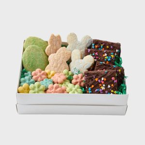 A box contains assorted cookies and brownies with colorful sprinkles, surrounded by decorative green paper, arranged neatly against a plain background.