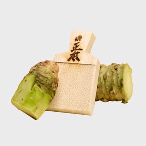 Wooden grater displays Japanese text, placed beside two fresh wasabi rhizomes on a plain background.