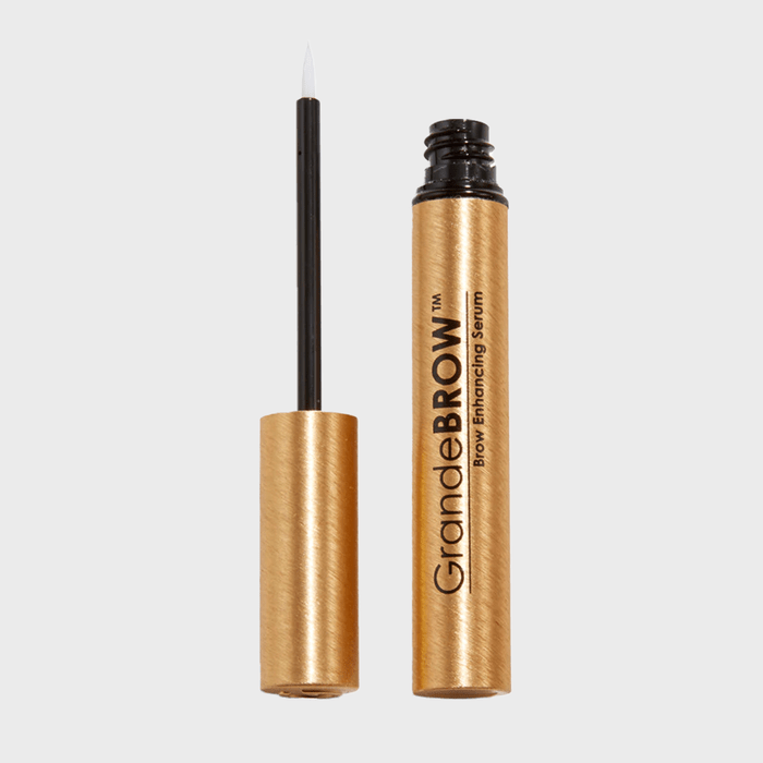 A gold tube stands open, revealing a fine brush. The label reads 