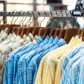 Shirts hang on wooden hangers, displayed on a metal rack in a clothing store. The shirts have various plaid and striped patterns.