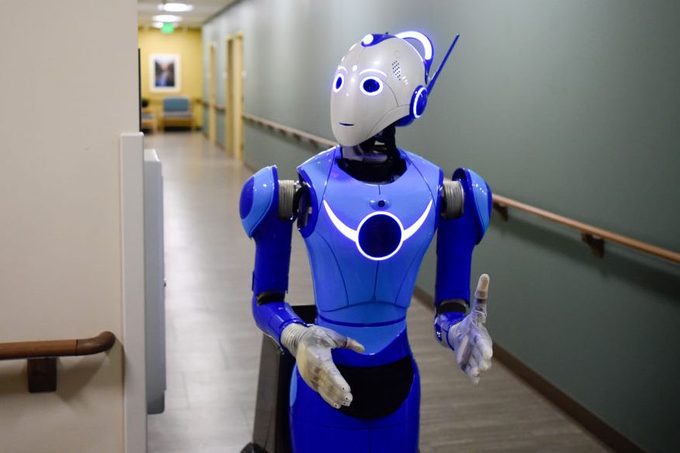 A humanoid robot walks down a hospital hallway, surrounded by green walls and wooden railings, conveying a futuristic healthcare environment.
