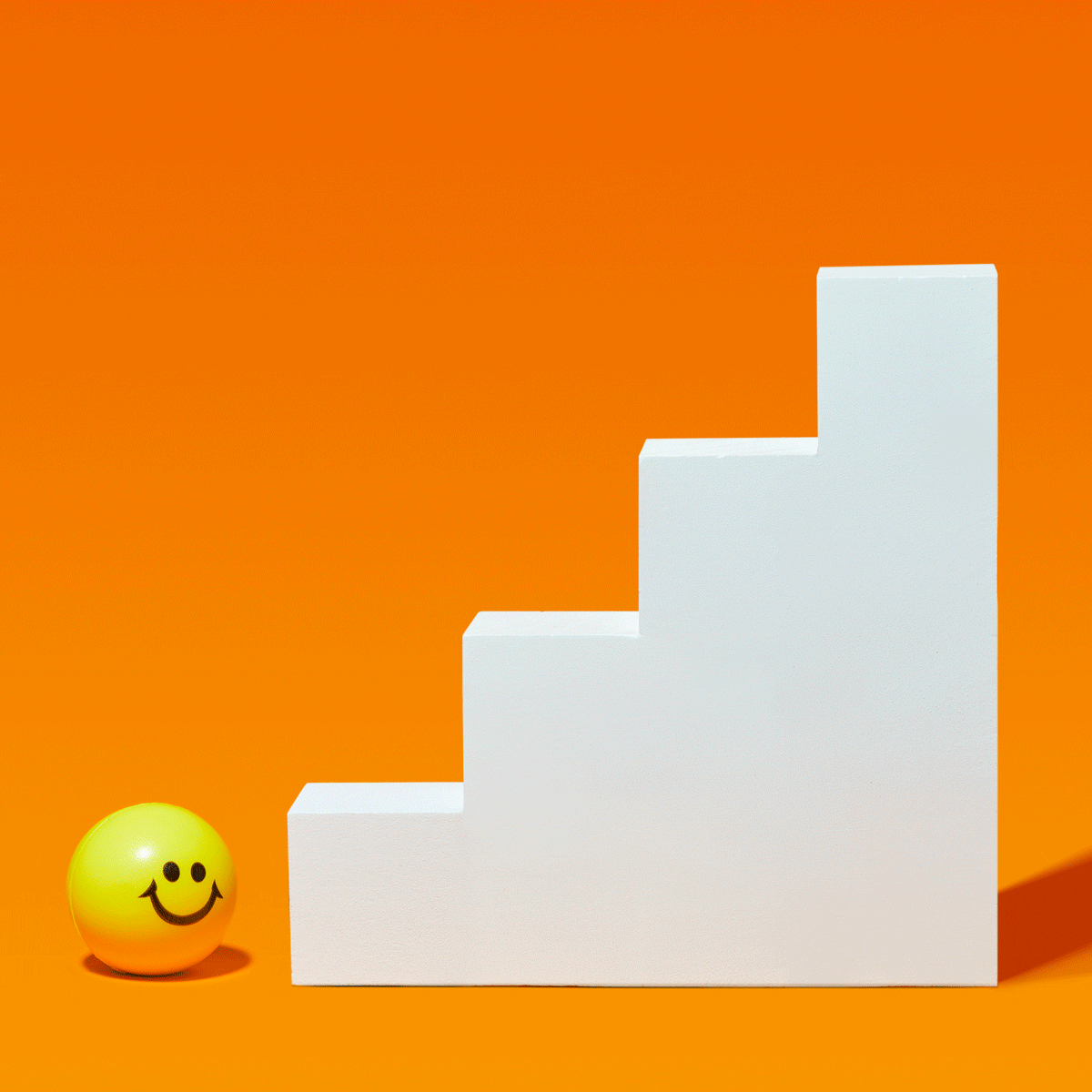 Yellow smiley face ball approaches white staircase against an orange background.