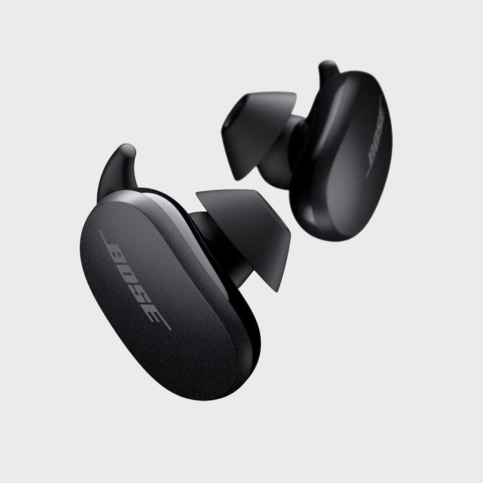 Black wireless earbuds floating against a plain, light gray background; one earbud displays the text 