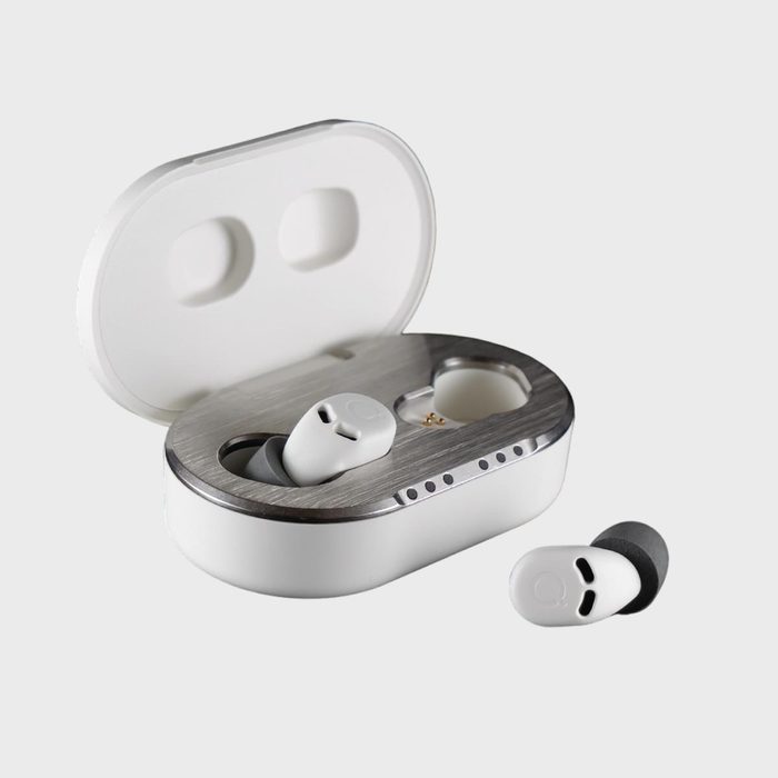 Earbuds rest in an open charging case, one earbud placed outside. The case has a metallic interior, set against a plain background.