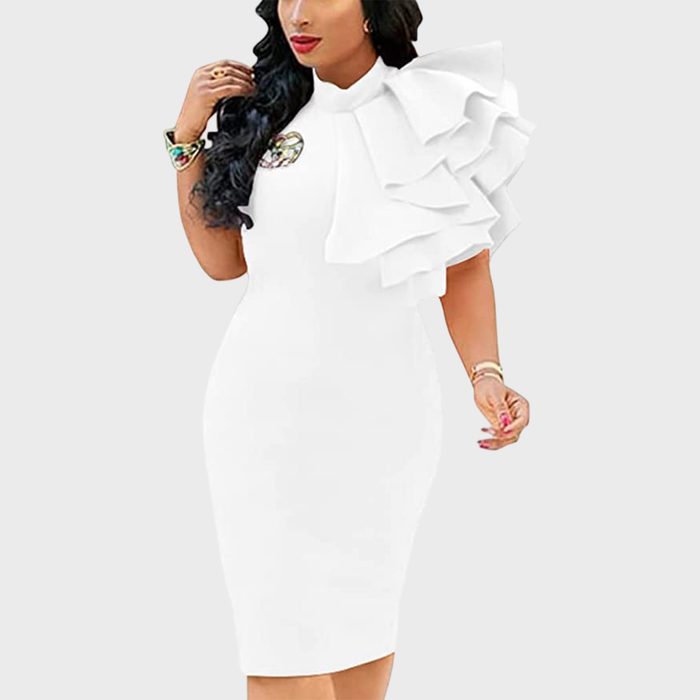 White dress features dramatic ruffled shoulder, worn by model posing against plain background, accessorized with jewelry and brooch on chest.