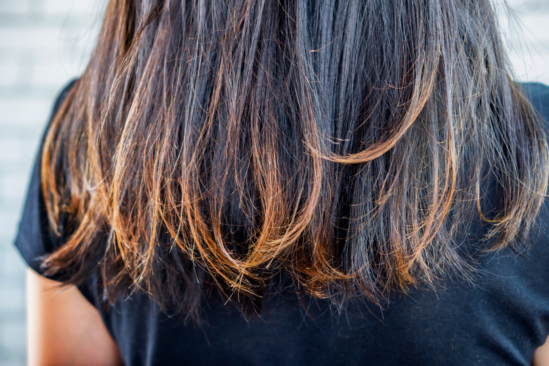 Brown hair flows over a black shirt, with a blurred light background.