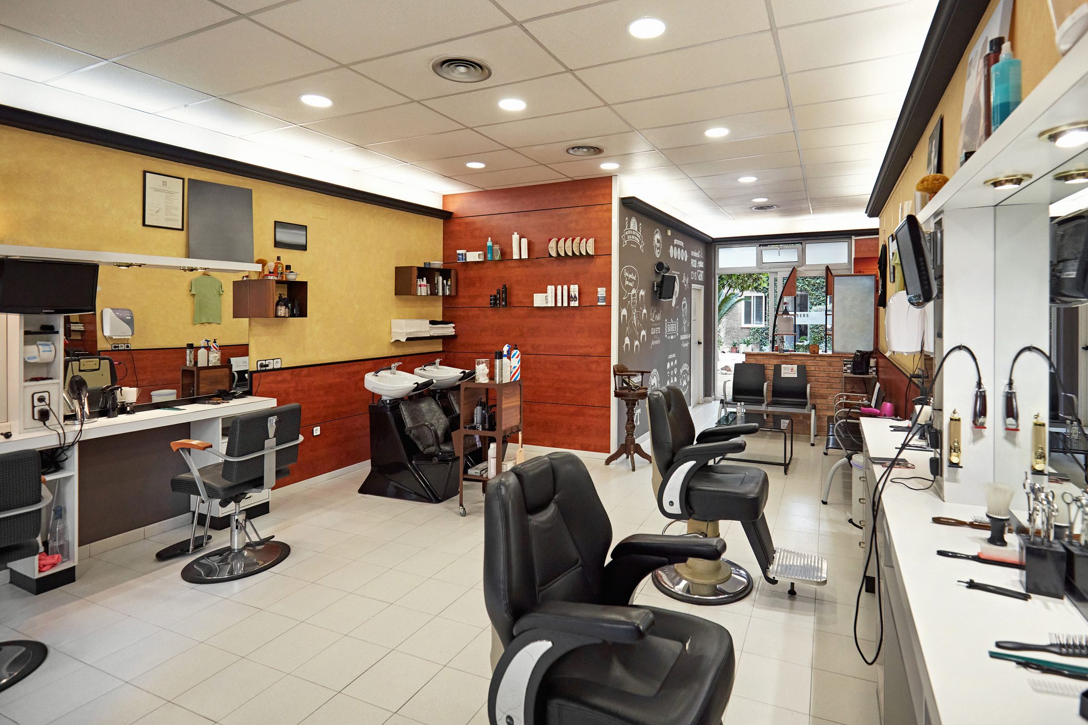 Barber chairs sit idle in a brightly lit barbershop with shelves of products, mirrors, and styling tools neatly arranged.