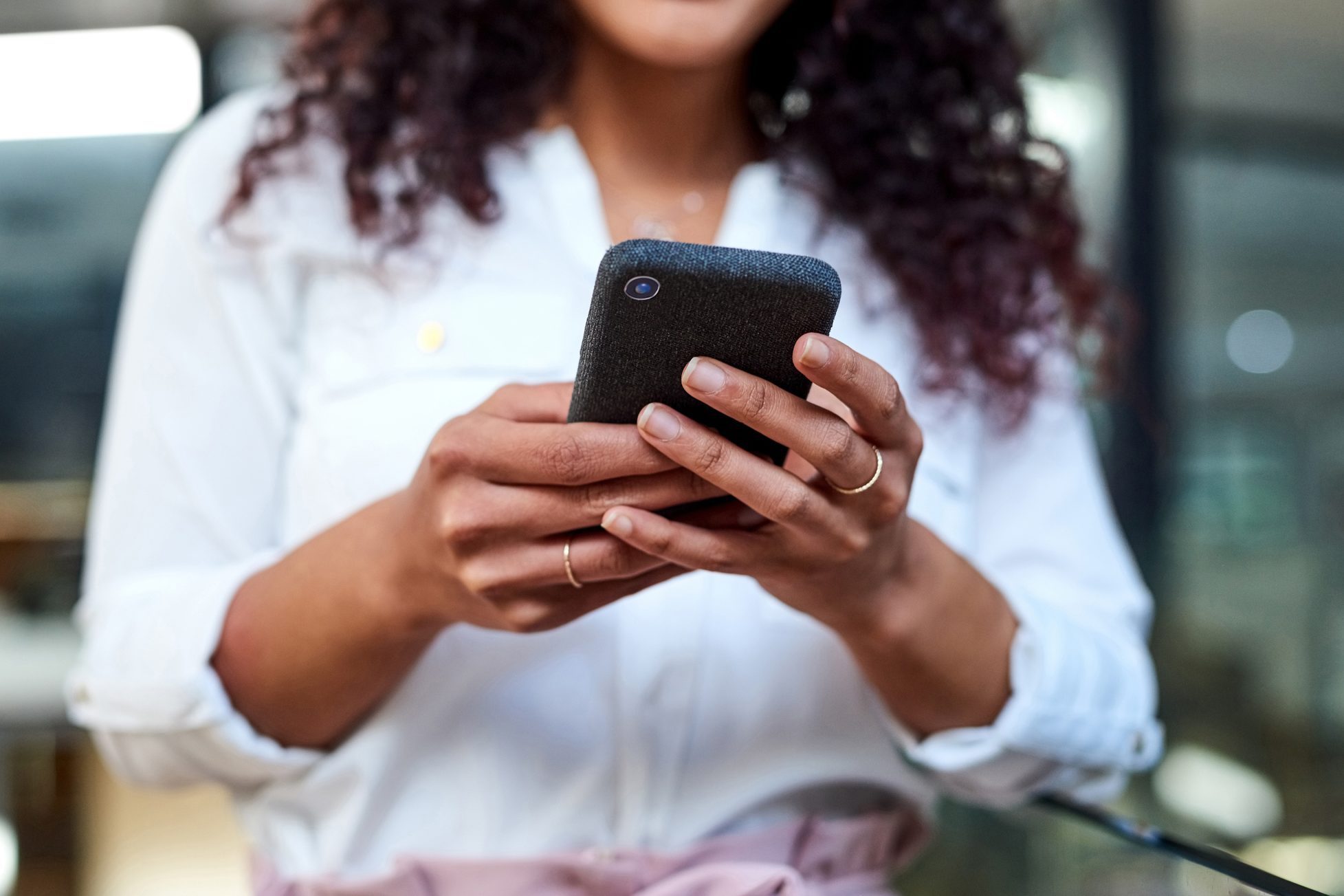 Person holding a smartphone, looking at the screen, with a blurred office background.