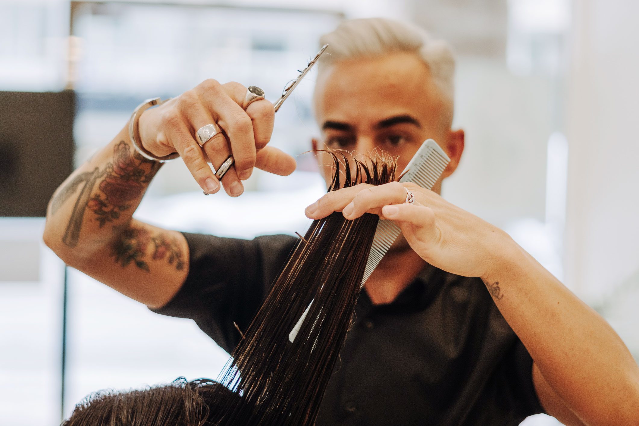 Hairdresser cuts wet hair using scissors and a comb in a brightly lit salon.