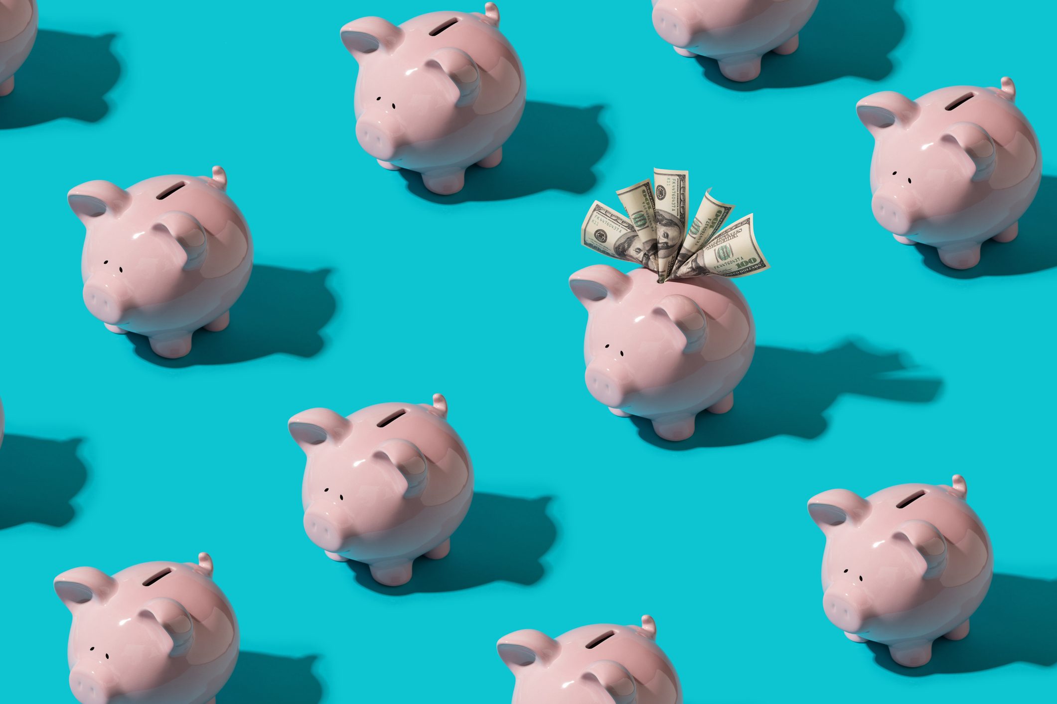 Piggy banks on turquoise background; one has dollar bills sticking out.