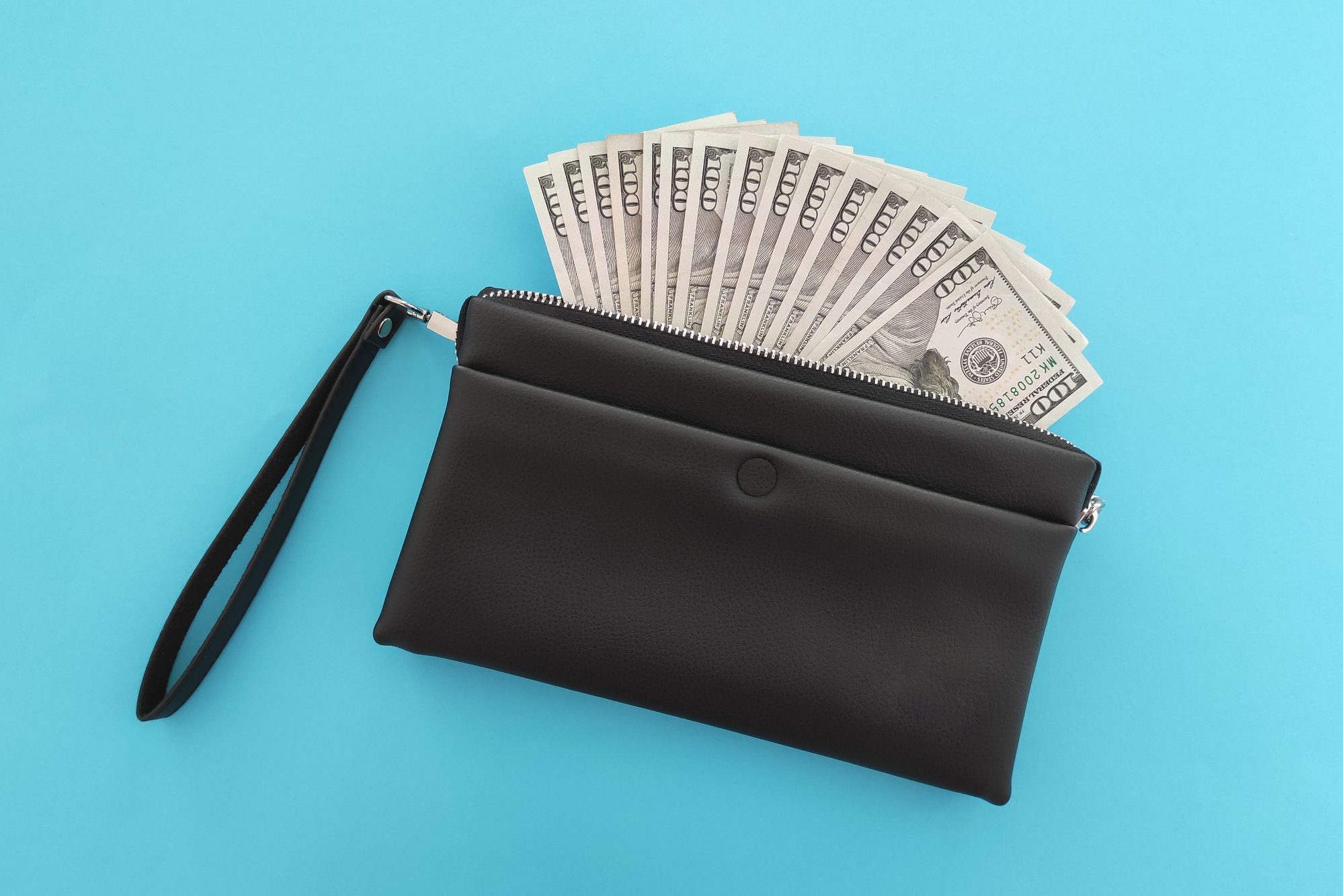 A black wallet partially unzipped revealing a fan of hundred-dollar bills, set against a plain blue background.