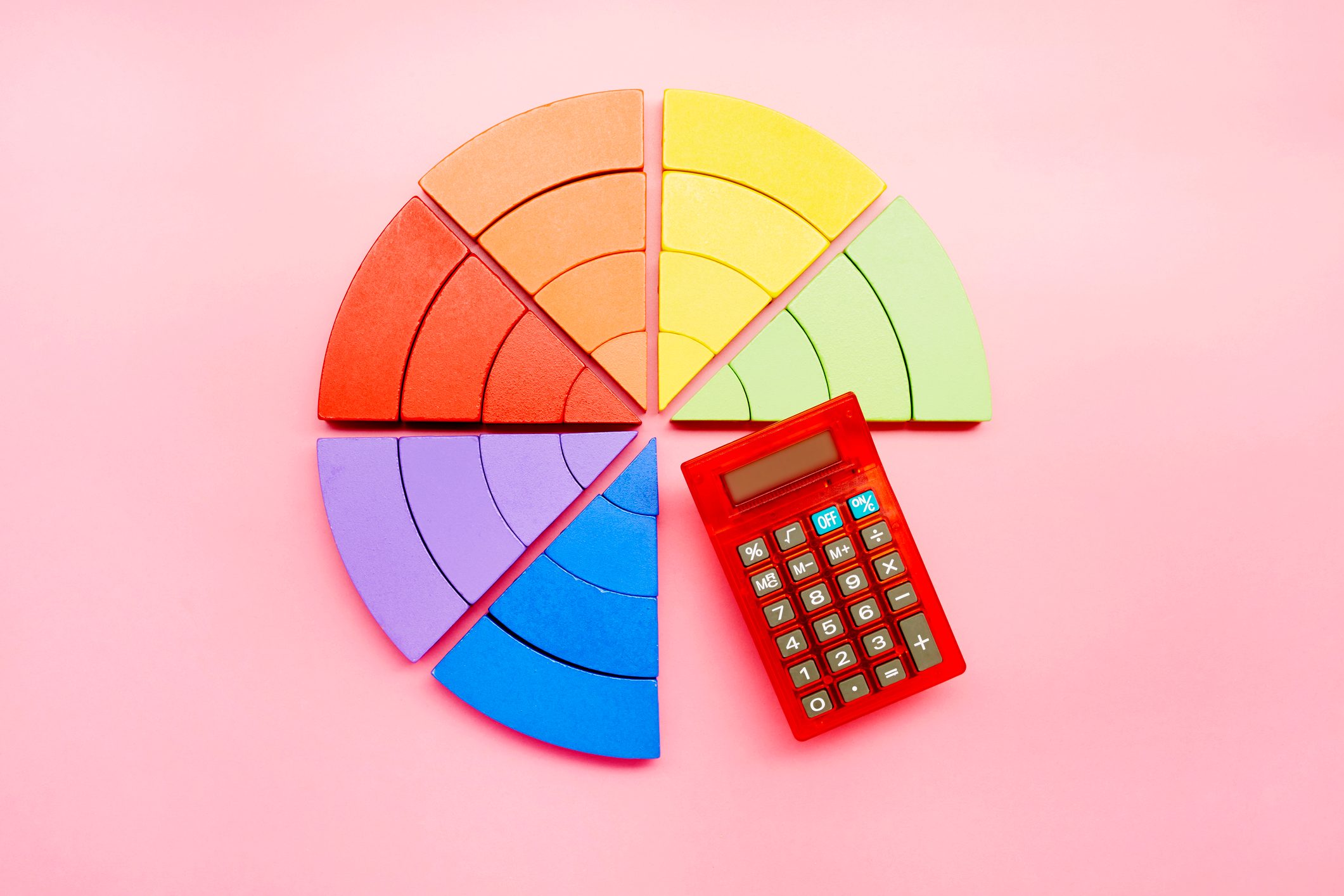 Colorful pie chart segments arranged on a pink background, with a red calculator placed next to them.