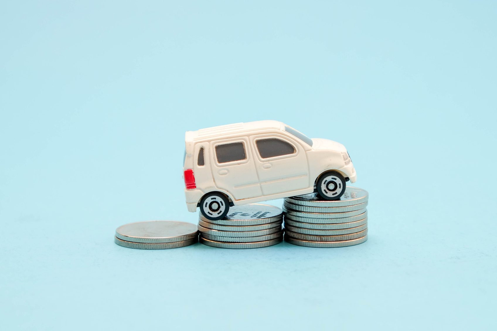 A toy car balances on stacked coins against a plain blue background.